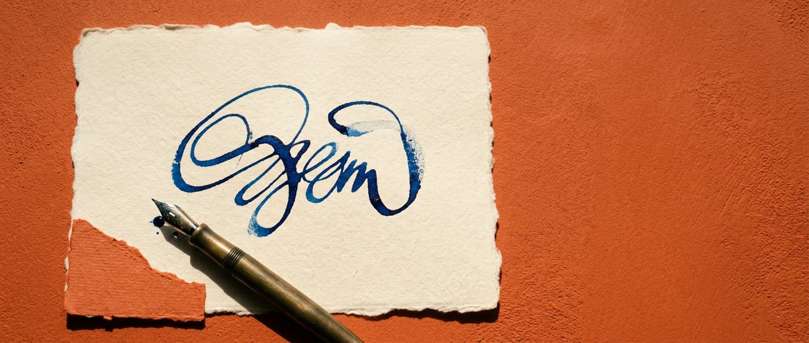 A fresh ink-blue signature drying on a sheet of cream deckled-edge paper, the nib of a fountain pen resting beside it.