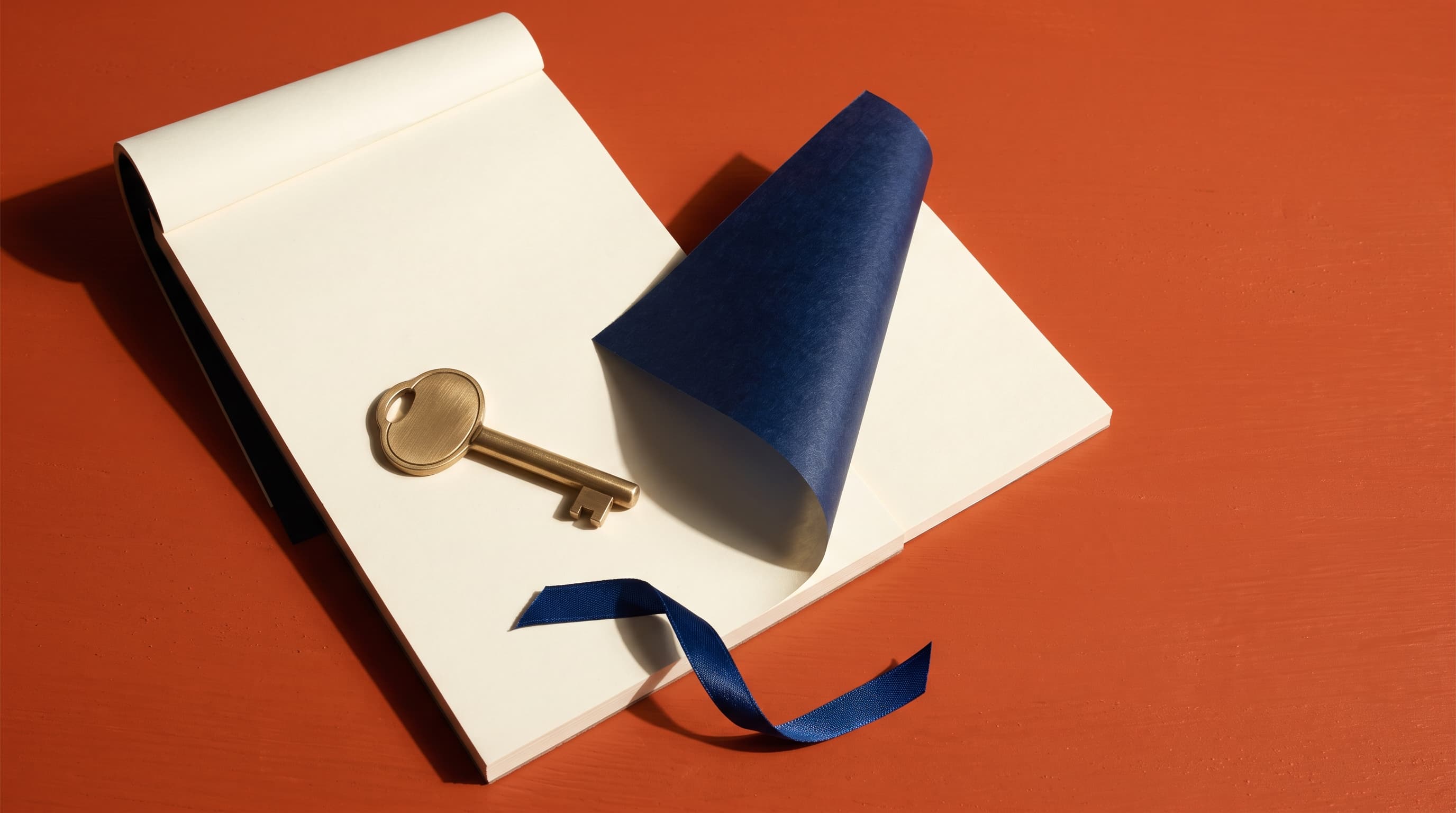 A blank cream duplicate receipt pad open on a terracotta surface, its deep blue carbon interleaf lifted to reveal the identical second copy beneath, with a plain brass key and a length of blue ribbon resting on the top sheet.